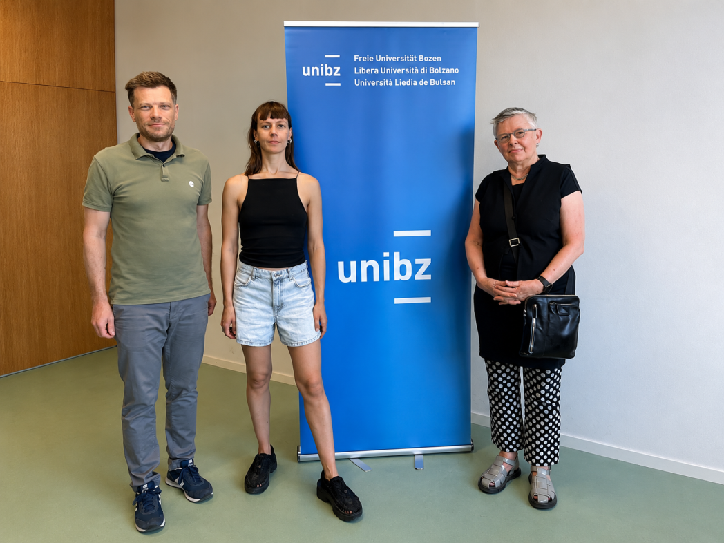 Prof. Richard Lang, Prof. Linda Andersen and Dr. Sophie Kallehauge pose for a picture in front of the unibz banner