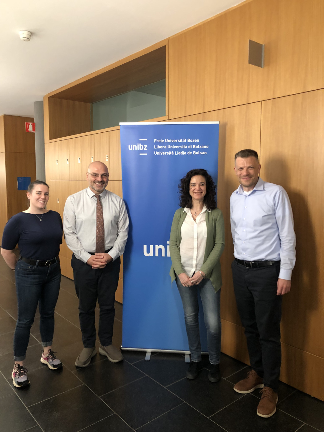 smiling people that pose next to the unibz banner