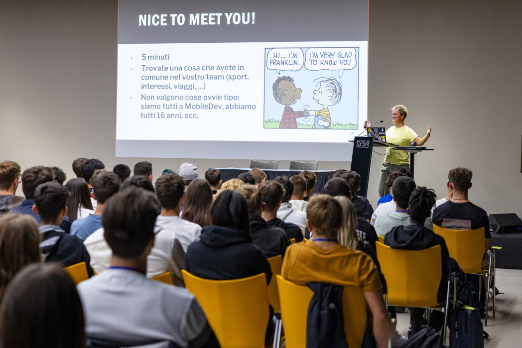 Un'aula piena, in cui gli studenti sono visibili da dietro. Davanti, la professoressa Ilenia Fronza è in piedi a un podio. Sul muro dietro di lei viene proiettata una diapositiva