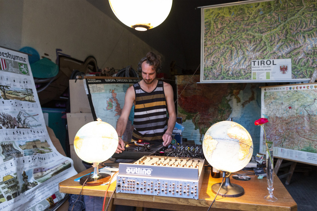 Mann steht hinter einem Mischpult. Landkarten befinden sich im Hintergrund.