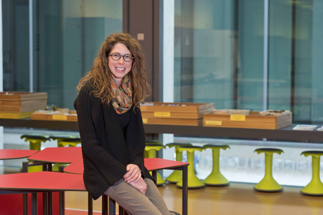 Donna sorridente seduta su un tavolino rosso in ambiente moderno.