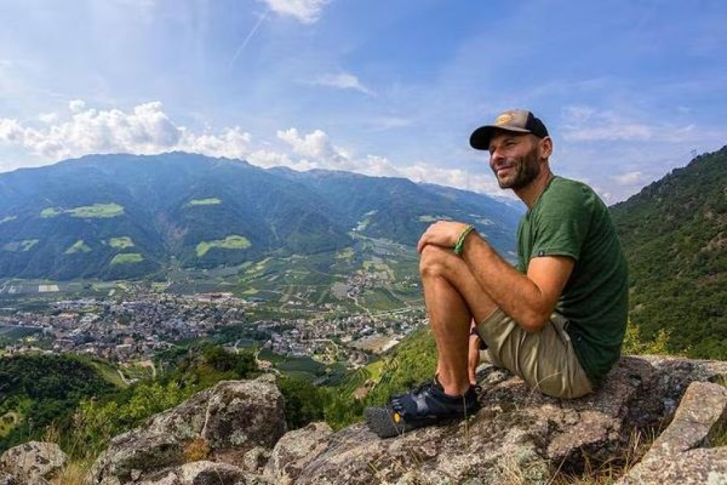 Mann sitzt auf einem Felsen. Im Hintergrund der Blick auf einem Tal. 