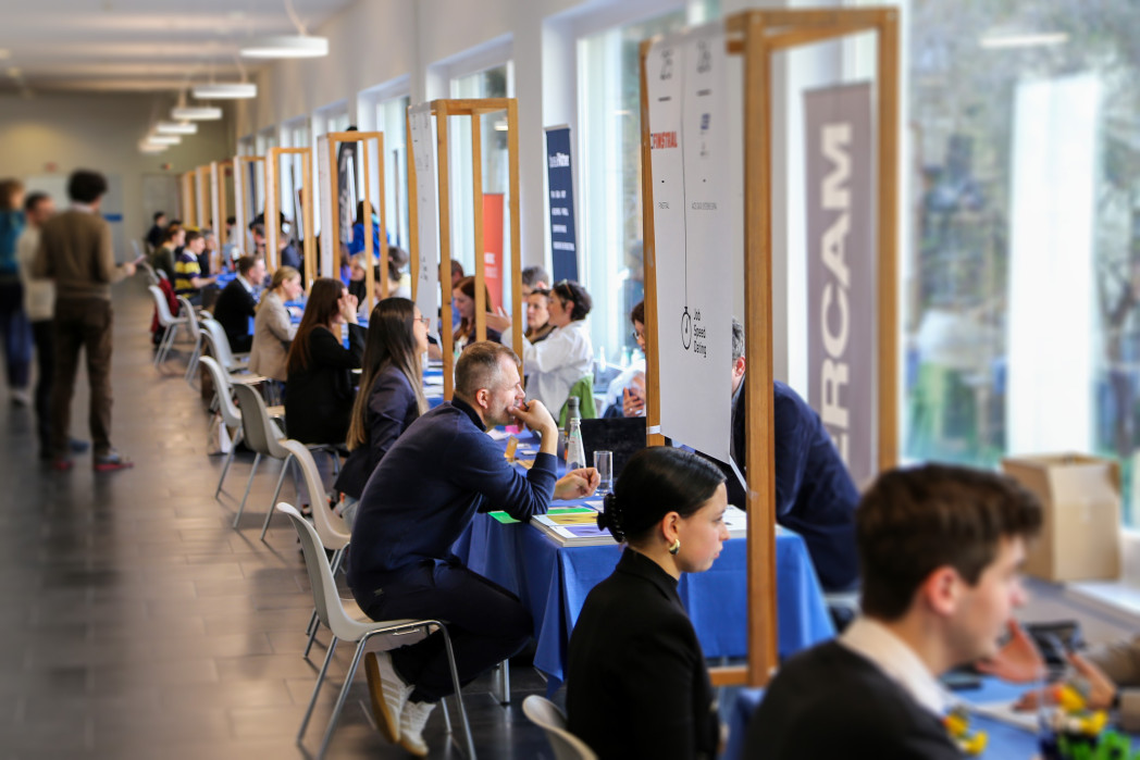Persone sedute ai tavoli in una lunga sala parlano tra loro durante un evento di networking o carriera.