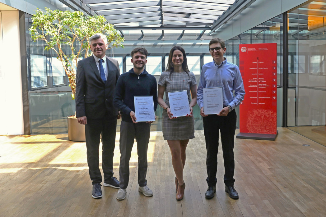 Quattro persone in posa; tre mostrano certificati in un edificio luminoso