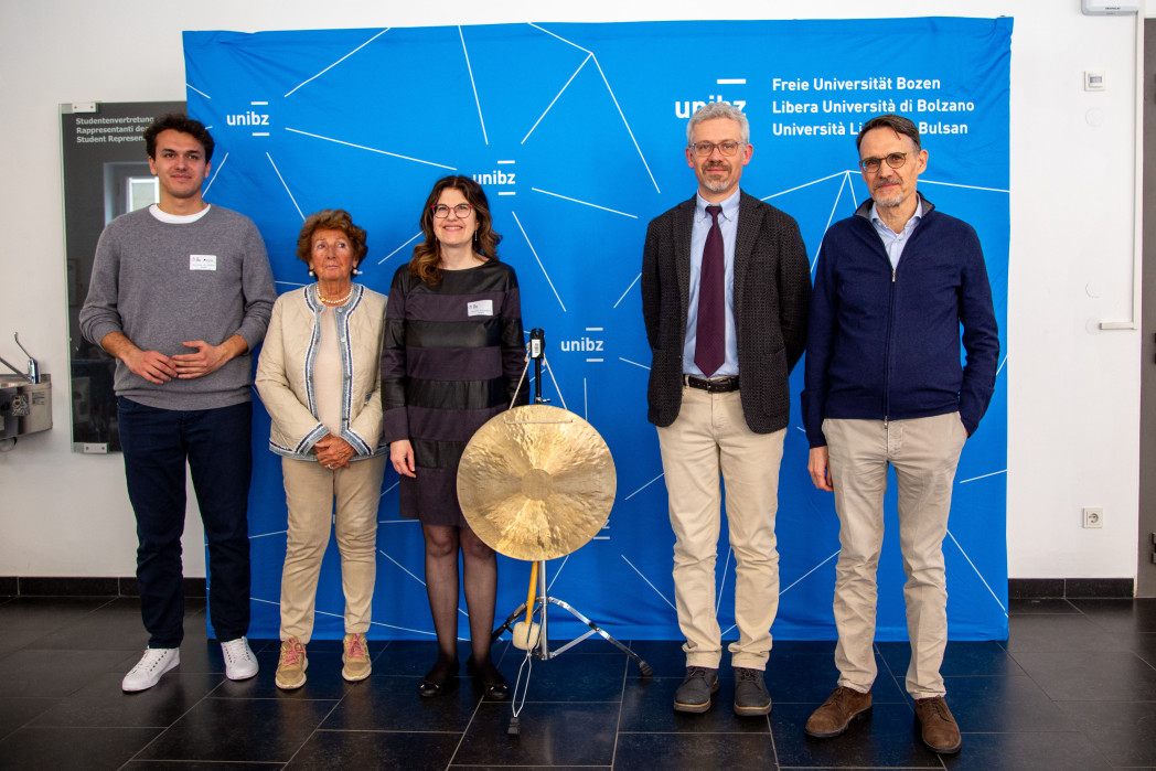 Cinque persone sorridono alla fotocamera. Sono in piedi davanti a un roll-up. Al centro c'è un gong.