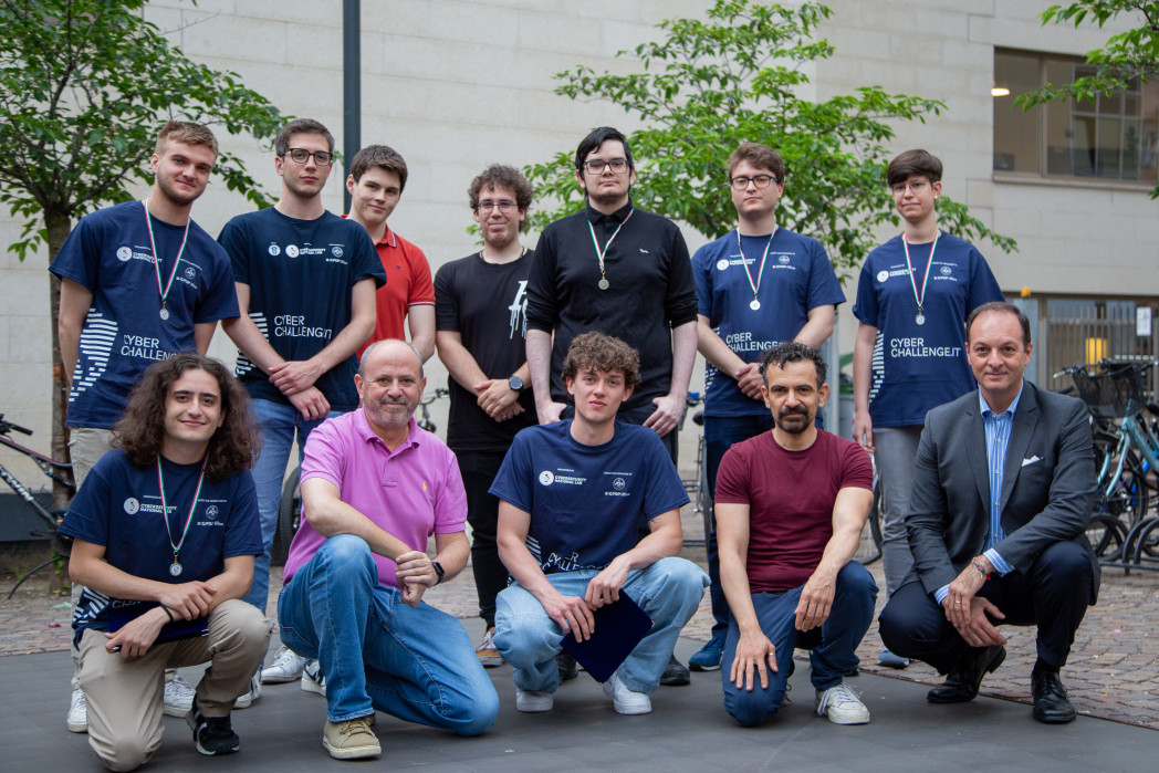 Gruppo di 12 persone in posa in piazza davanti all'edificio dell'università. Tutti sorridono.
