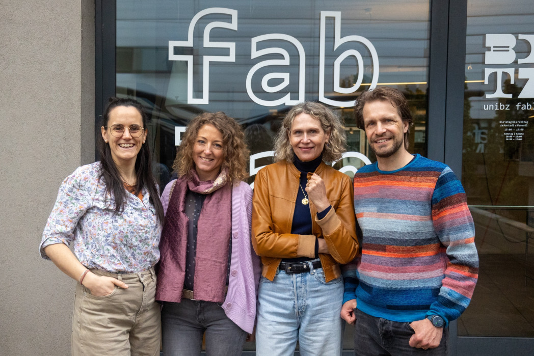 drei Frauen und ein Mann stehen for einer Glasscheibe mit der Aufschrift fab