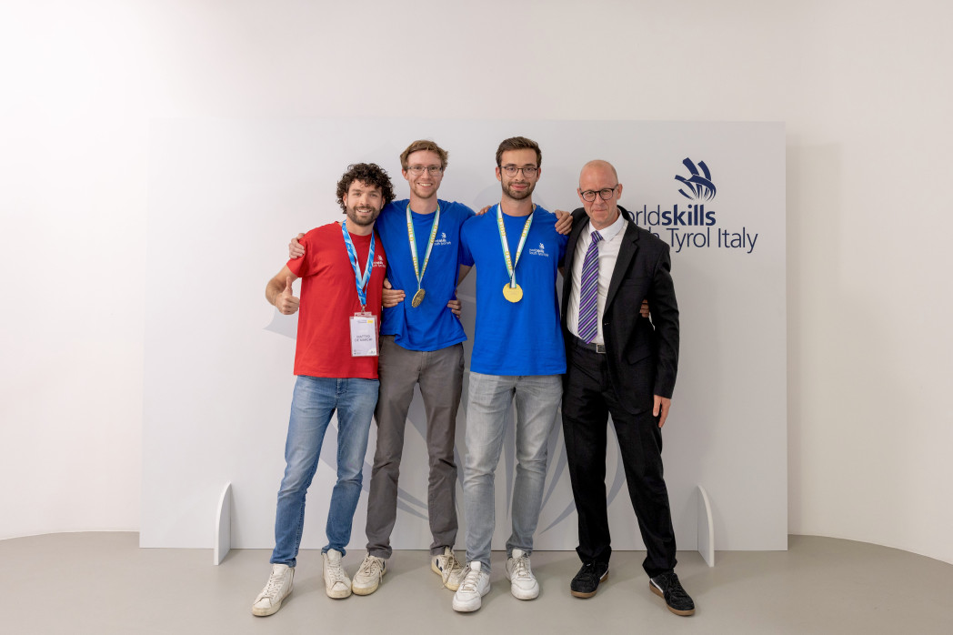 Vier Männer posieren vor dem „Worldskills South Tyrol Italy“-Logo, zwei mit Medaillen.