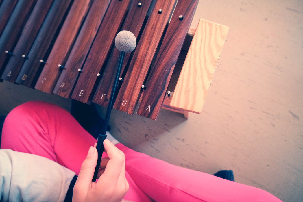 Ein Kind spielt mit einem Schlägel auf einem Xylophon aus Holz.