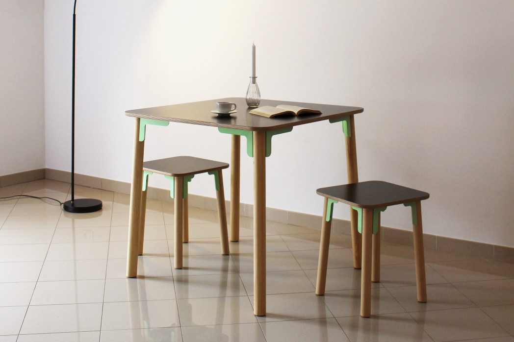 Quadratischer Tisch mit zwei quadratischen Hockern aus Holz. Alle drei Möbelstücken werden mit je 8 Verbindungsstücken an ihrer Unterseite und den Tisch- und Stuhlbeinen zusammengehalten.