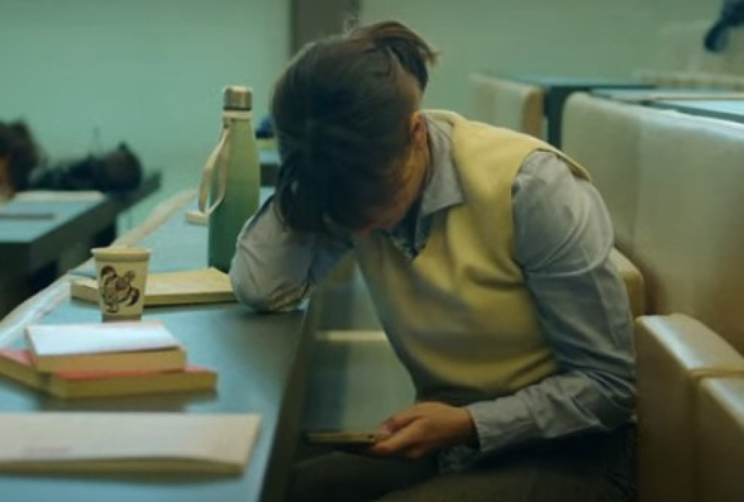 Persona con la testa abbassata seduta a una scrivania con libri e documenti.