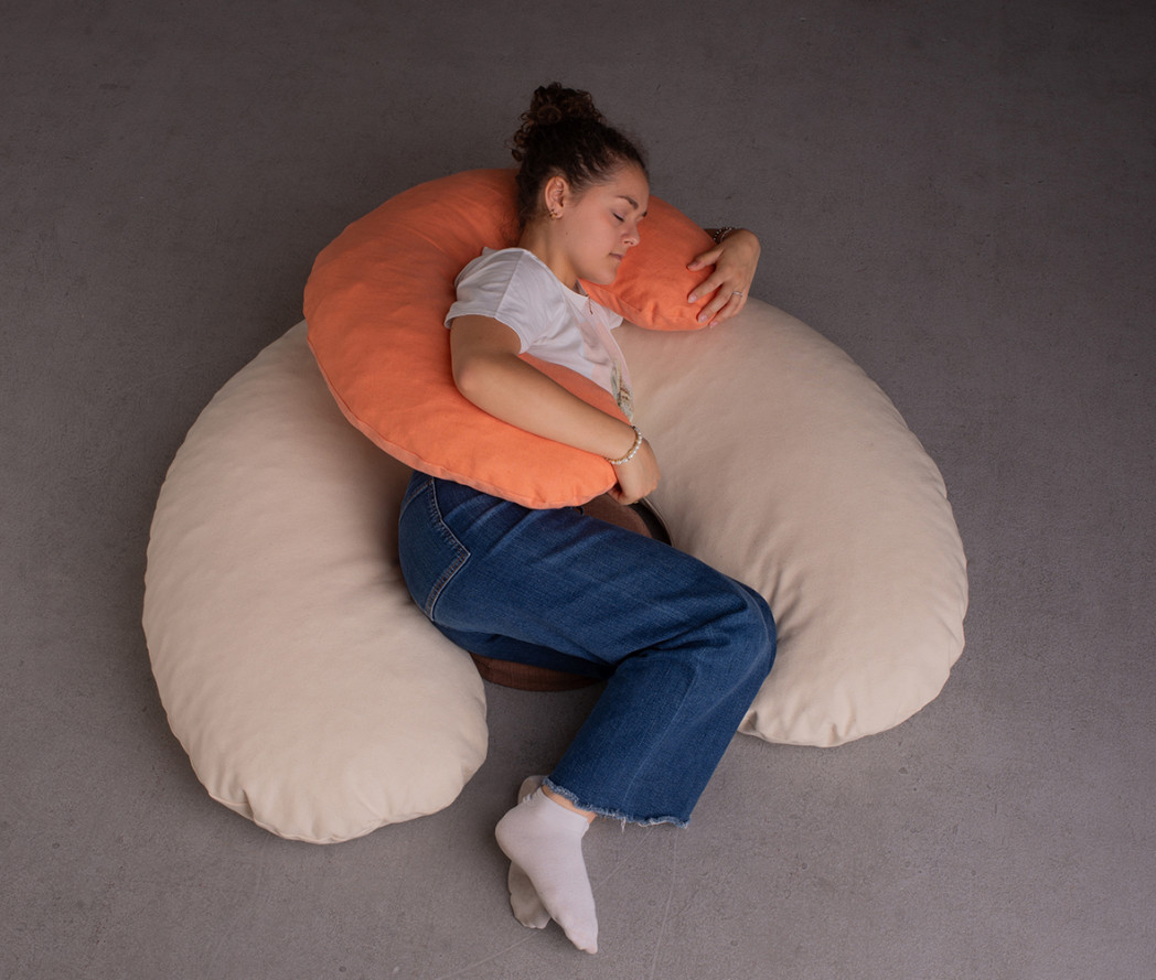 Donna sdraiata su un grande cuscino ergonomico, abbracciando un cuscino più piccolo. Sembra rilassata e addormentata.