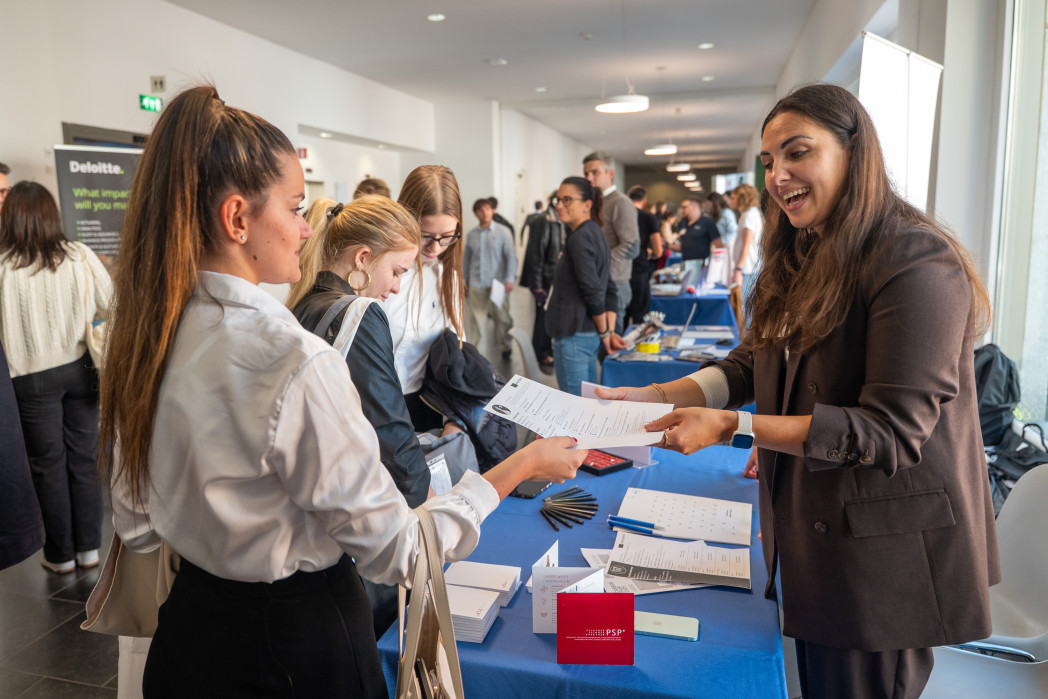 Due donne che parlano a un tavolo informativo durante un evento con partecipanti sullo sfondo