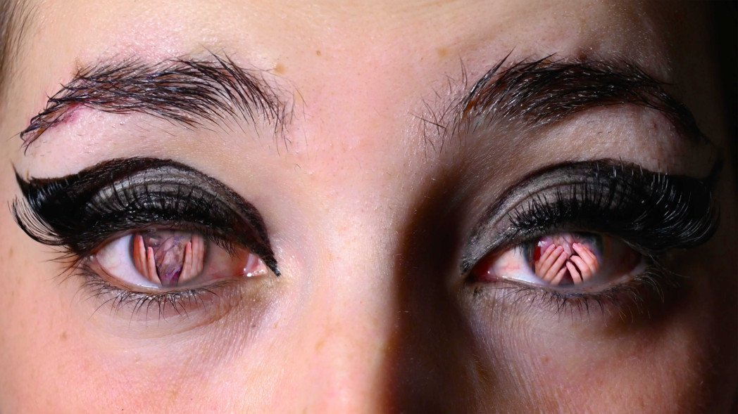 Ausschnitt eines Gesichts mit Augen und Brauen, stark geschmickt und in der Iris spiegeln sich Hände .