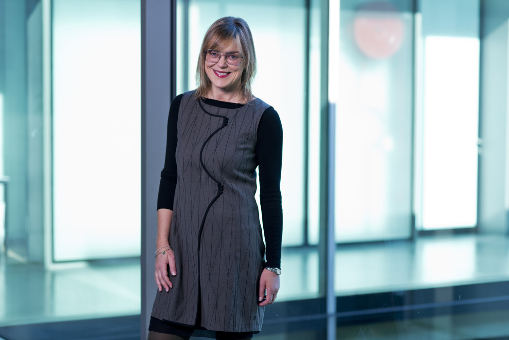 Donna sorridente con occhiali in elegante abito nero in piedi in ufficio moderno con parete di vetro.