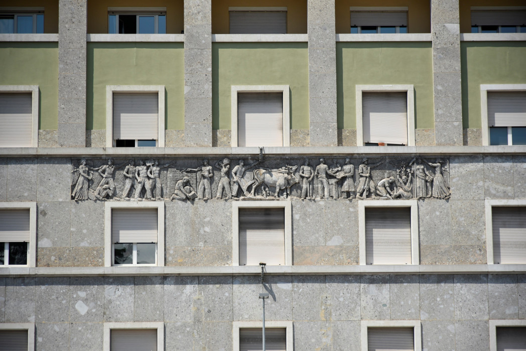 Fassade eines Gebäudes mit mehreren Fenstern und einem Steinfries, das Figuren in Bewegung darstellt.