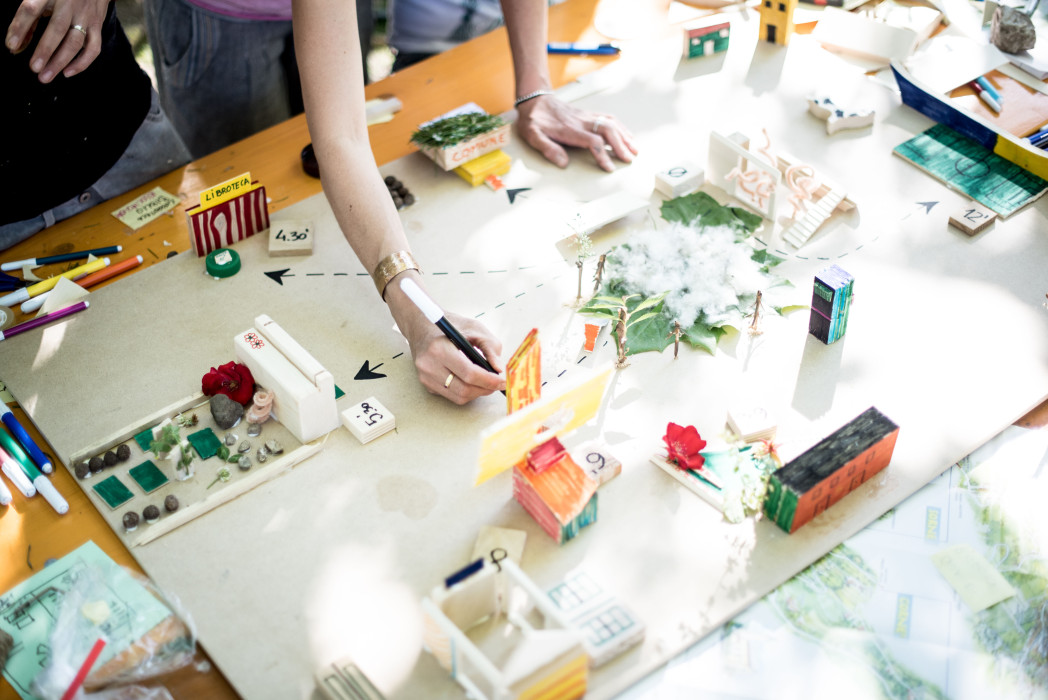 Mani di più persone che lavorano su modelli architettonici colorati e progetti di edifici su tavolo da lavoro bianco.