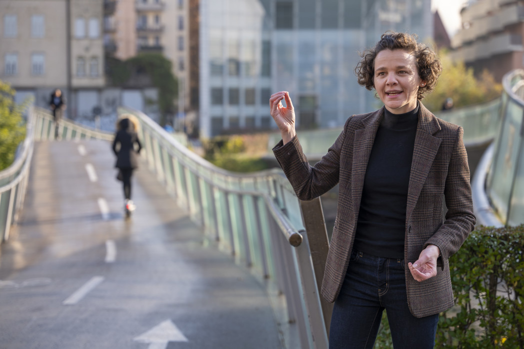 Frau steht vor einer Brücke mit Gebäude dahinter und gestikuliert bei Sprechen