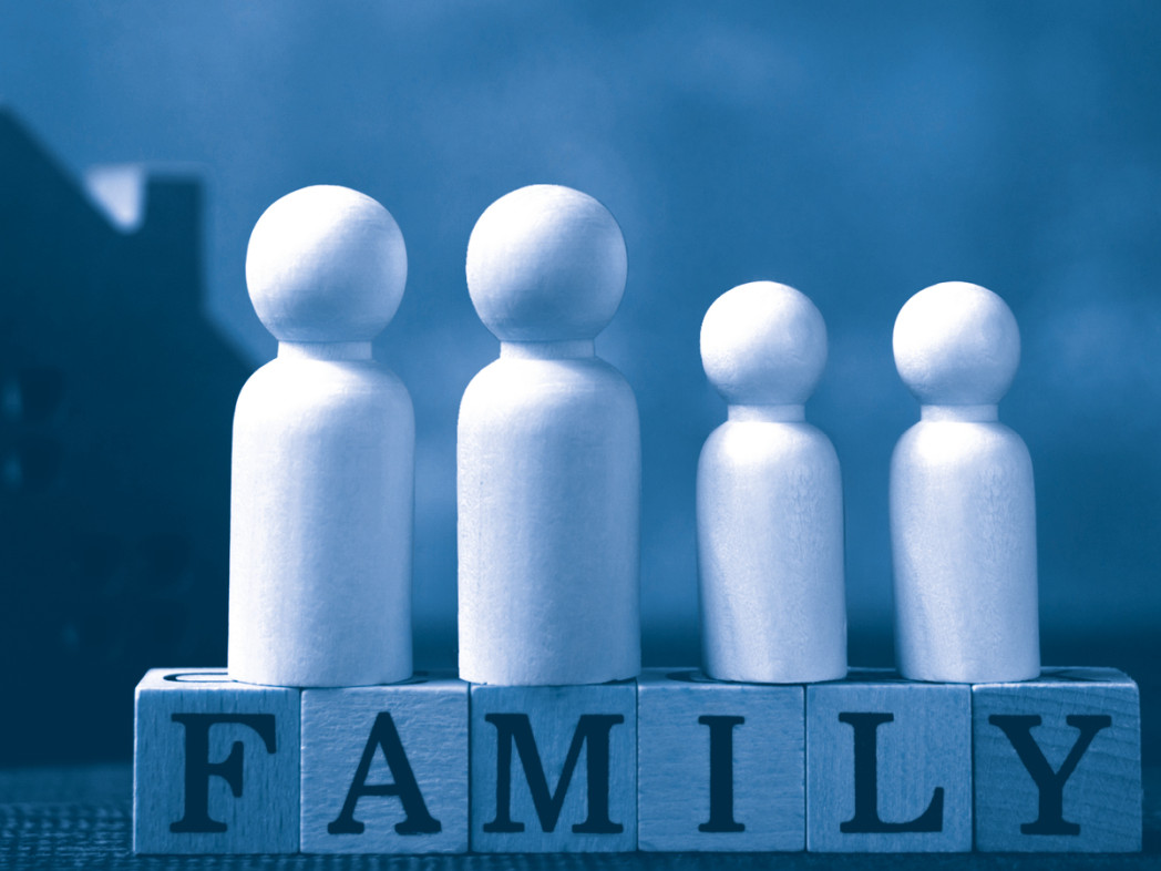 Raffigurazione simbolica di una famiglia con quattro figure di legno su cubi che formano la parola “FAMILY”; sullo sfondo la sagoma di una casa.