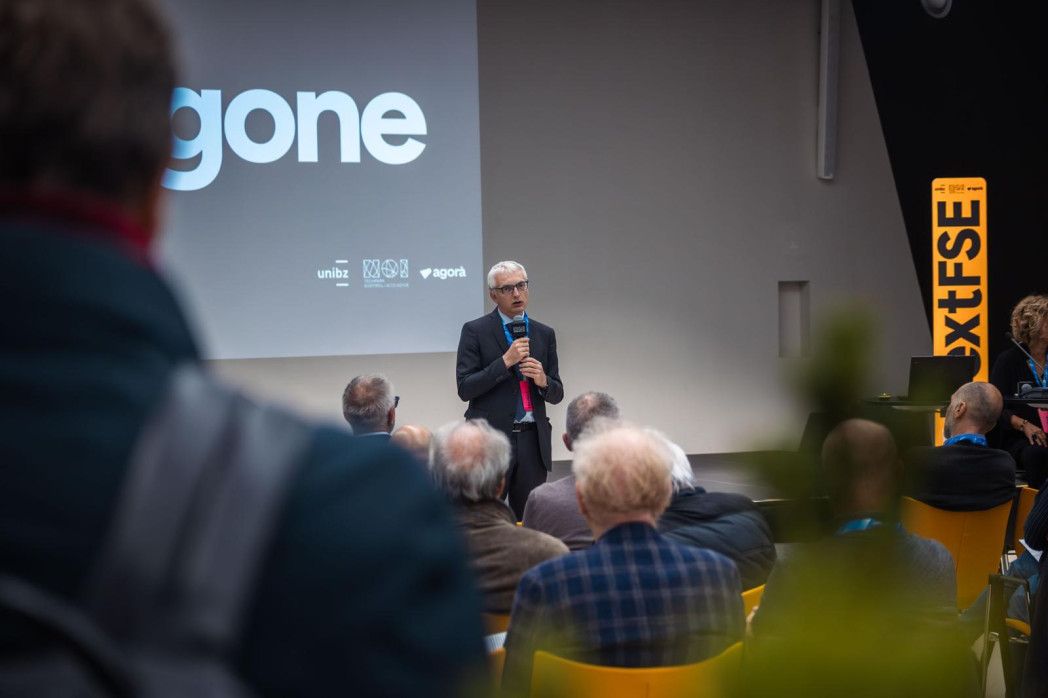 Speaker presenting to seated audience in conference room with projection screen