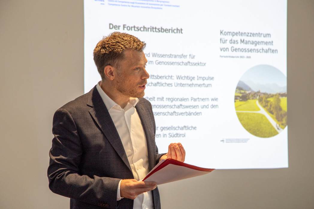 Uomo durante una presentazione su cooperative, con fascicolo rosso in mano.