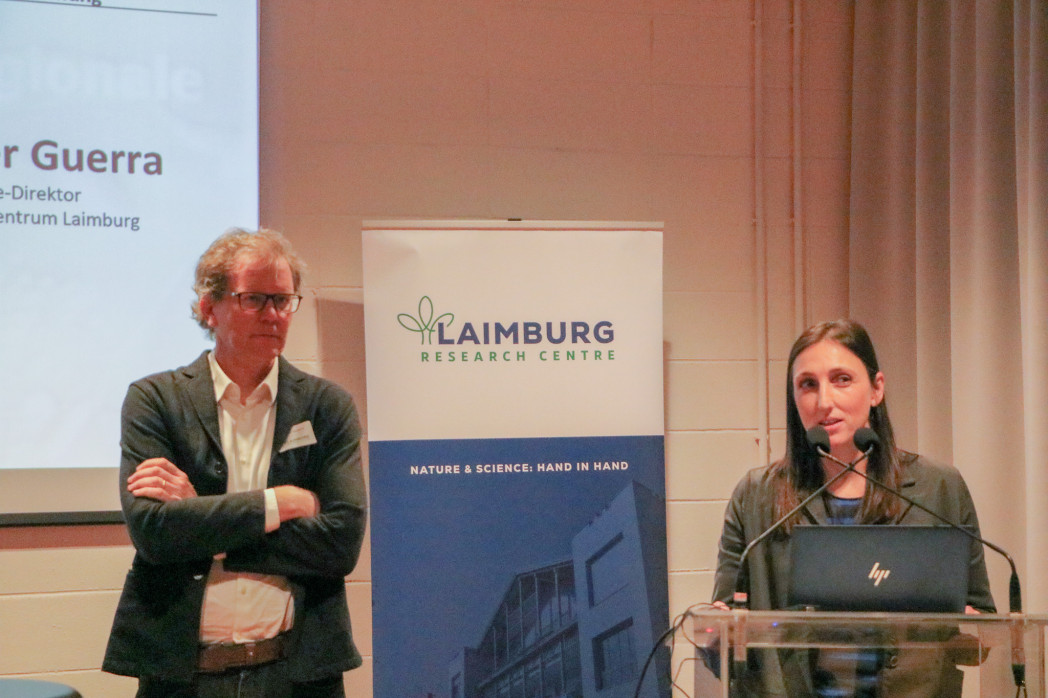 Zwei Vortragende stehen vor einem Banner des Laimburg Research Centre; die Frau spricht am Podium, der Mann steht daneben.
