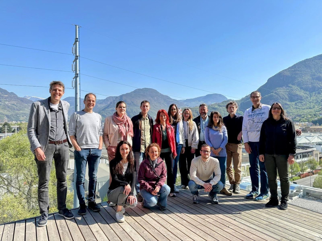 Gruppenfoto von 15 Projektbeteiligten auf einer Terrasse vor Bergkulisse bei sonnigem Wetter