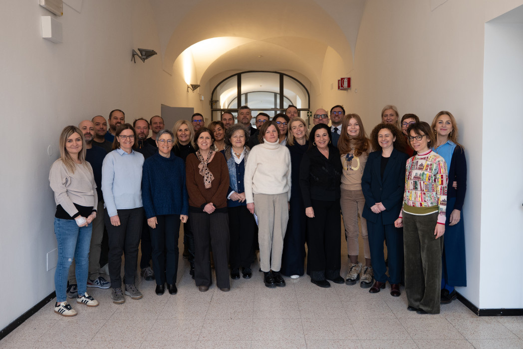 Foto di gruppo con circa 30 adulti in piedi uno accanto all’altro in un corridoio luminoso, sorridenti verso la fotocamera.