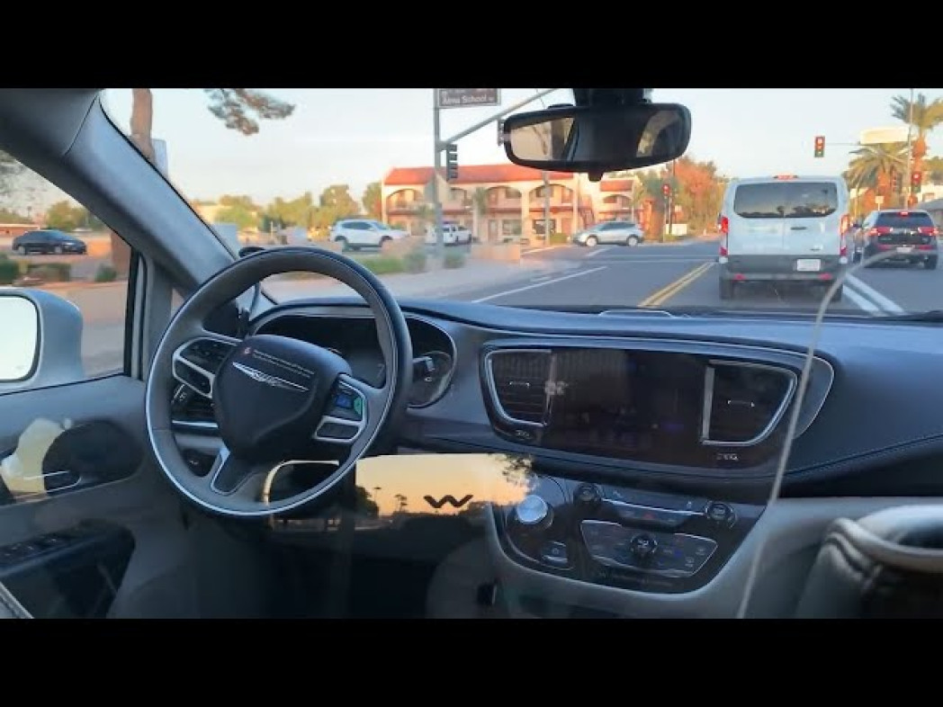 View from inside a car looking out at a street with buildings and traffic in the background.