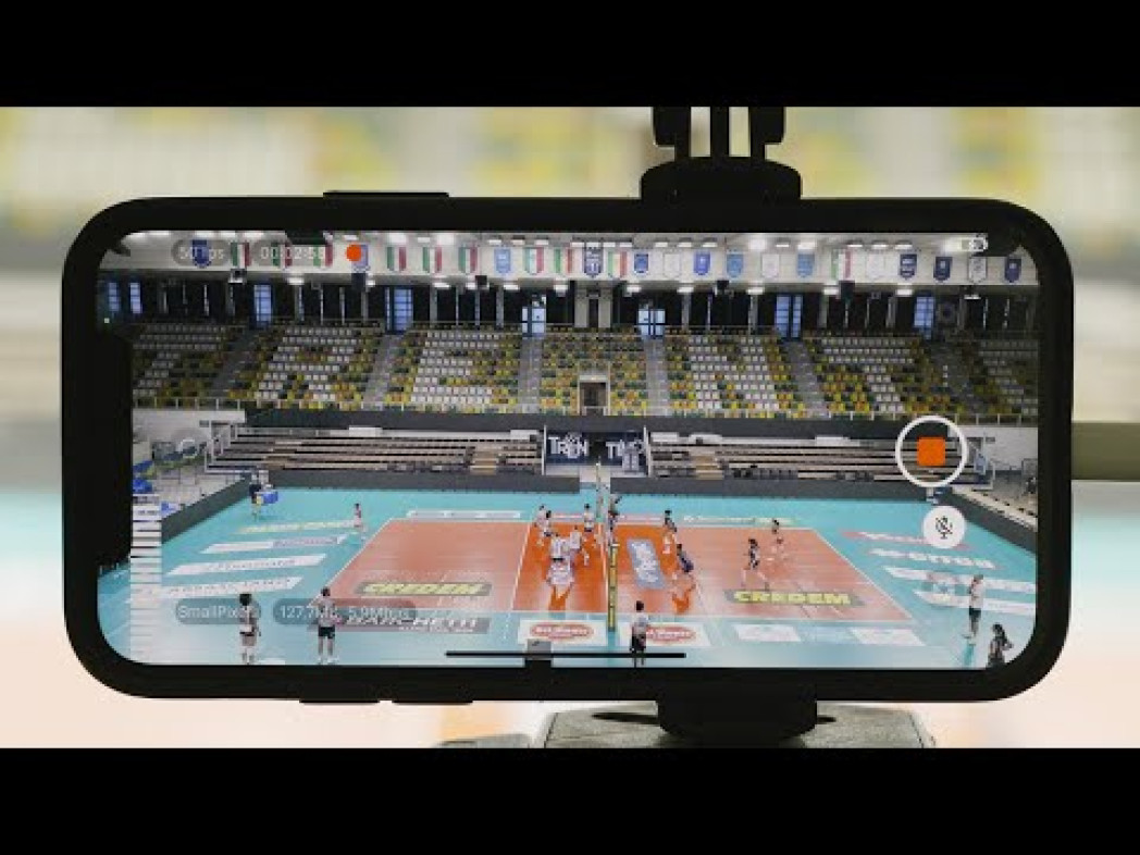 Uno smartphone montato su un treppiede riprende una partita di pallavolo in un palazzetto.