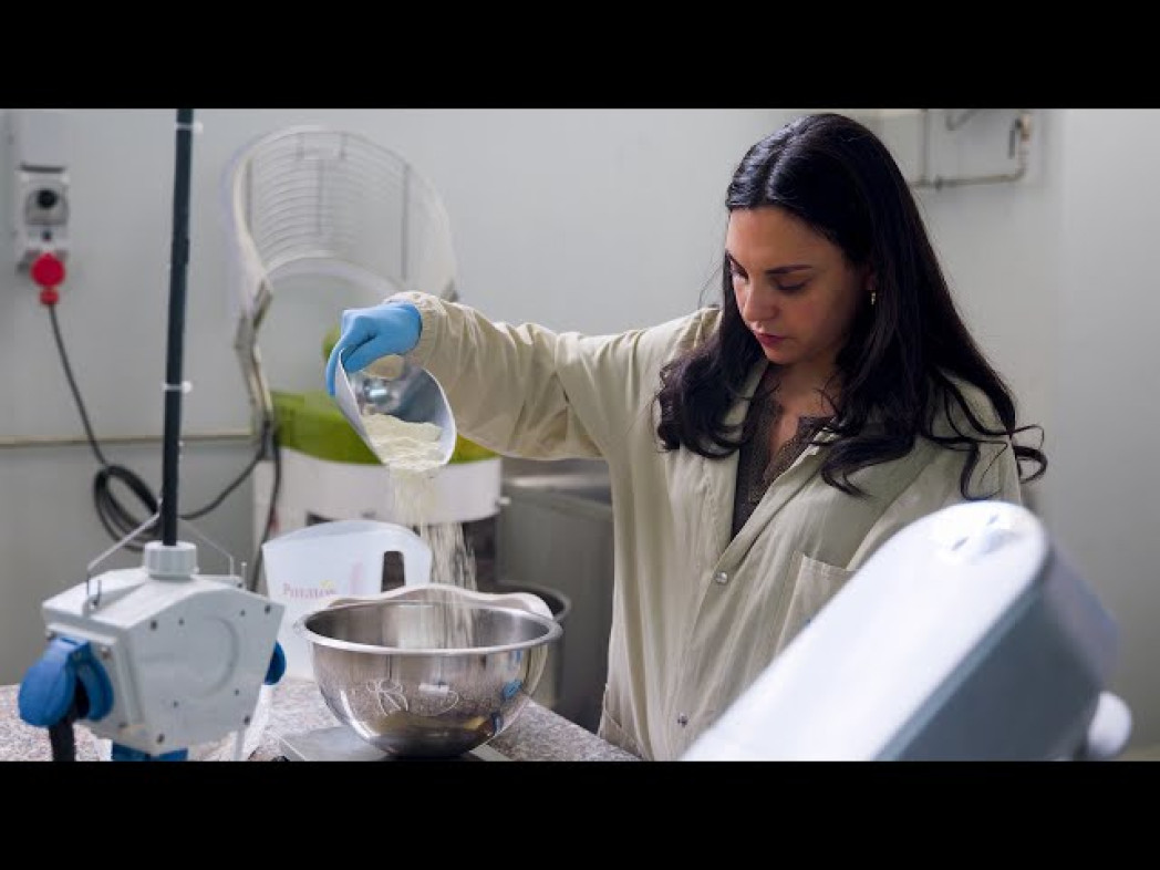 Female scientist in white lab coat pouring powdery material into a bowl in the laboratory.