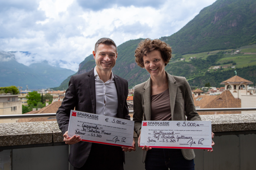 Due persone su una terrazza con assegni simbolici in mano.