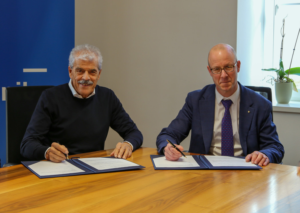 Due uomini in abiti formali che firmano documenti a un tavolo da conferenza in legno