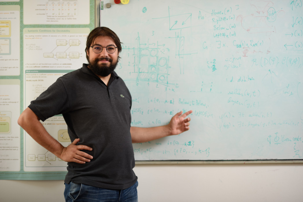 Man standing in front of a whiteboard with mathematical formulas, pointing at the board and smiling.