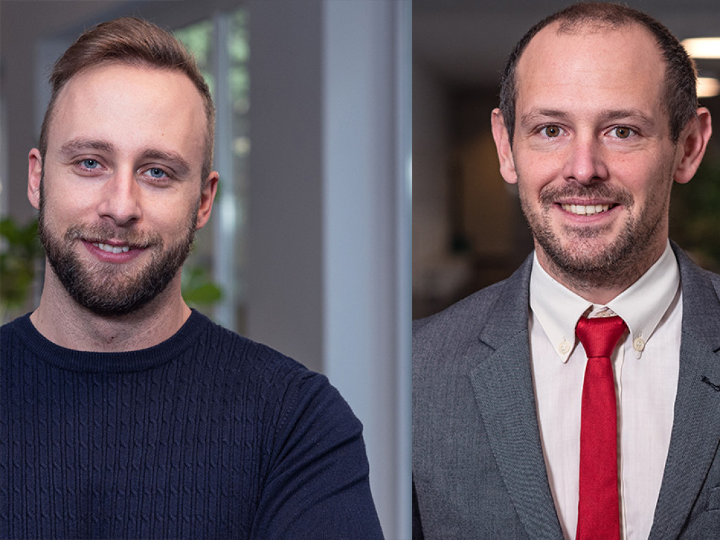 Two men photographed in a bust portrait in a modern setting. They are smiling at the camera.