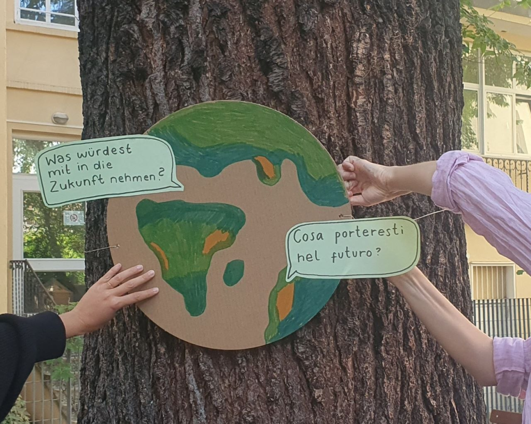 Un globo di cartone applicato a un albero, con fumetti che chiedono in tedesco e in italiano cosa portare nel futuro.