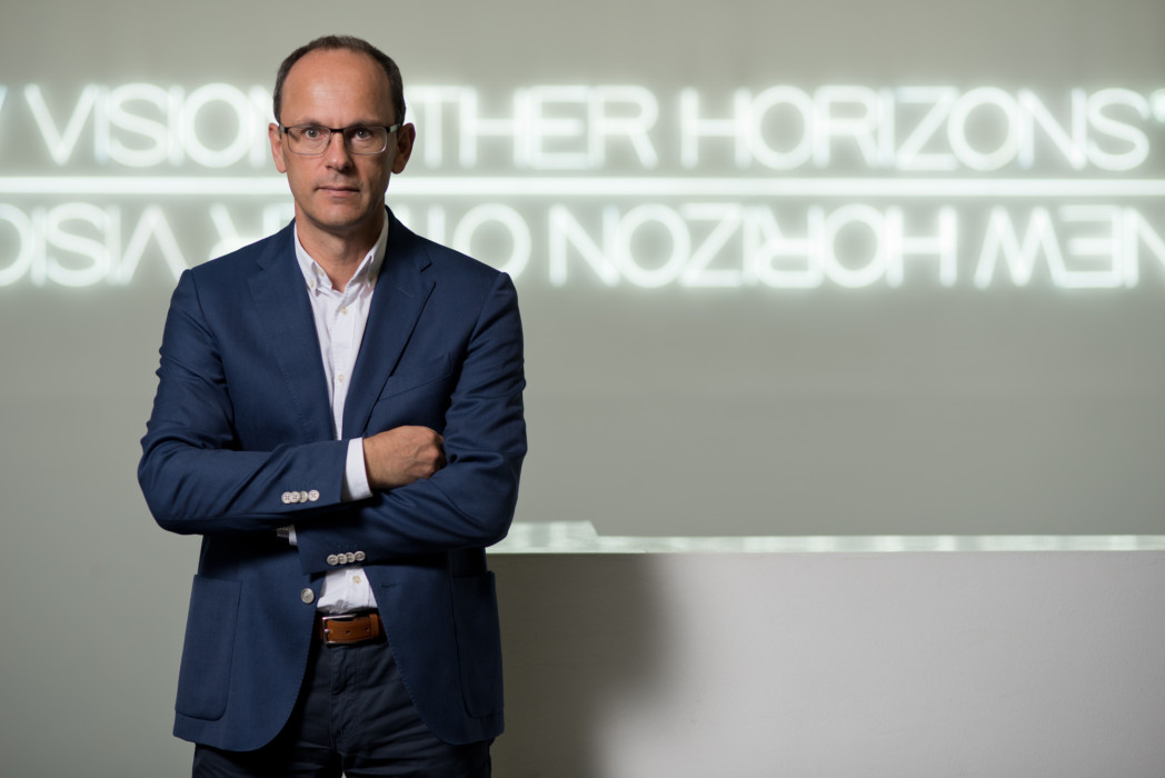 Professor Johann Gamper steht in einem Korridor vor einer Leuchtschrift.