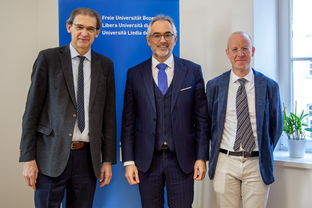 Drei Personen stehen vor dem Banner der Universität.