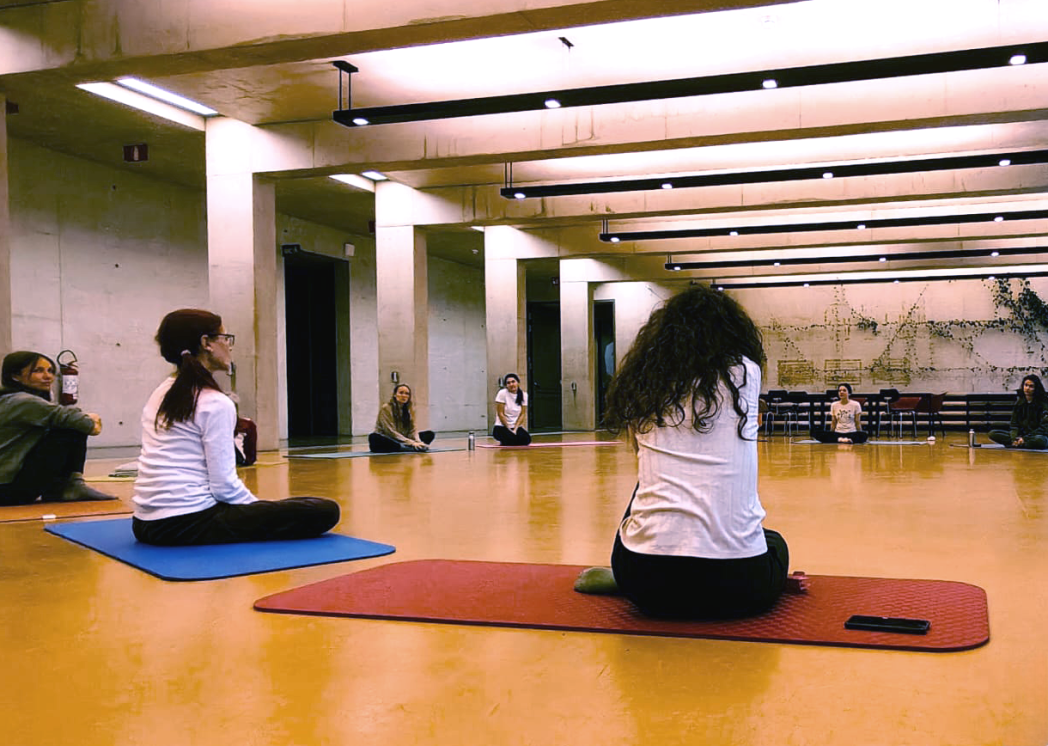 Persone sedute su tappetini da yoga in una sala spaziosa e luminosa.