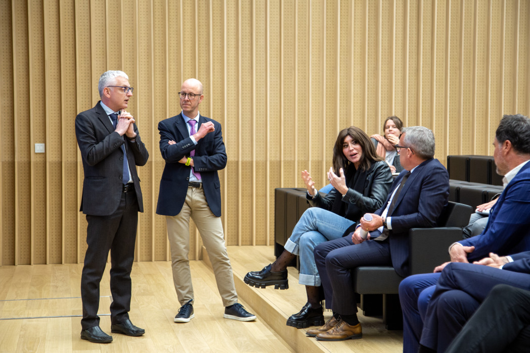 Due uomini parlano davanti a un piccolo pubblico in un’aula moderna.