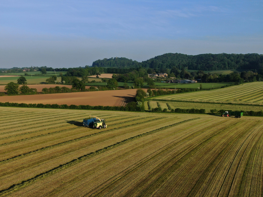 Vista aerea di campi coltivati con trattori al lavoro sotto un cielo sereno