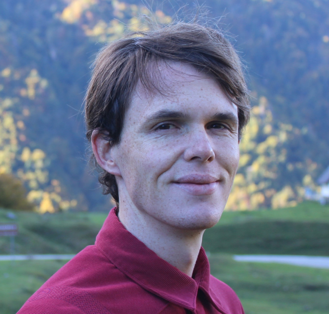 Portrait of a man outdoors with a forested mountain background.