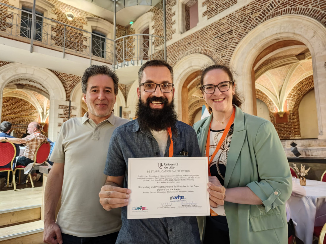 Three people smiling and holding a certificate in a historic indoor setting.