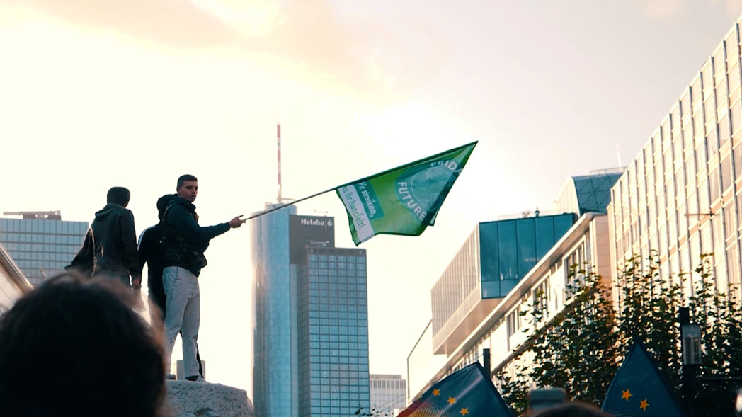 Person waving a green flag in a city surrounded by modern buildings.