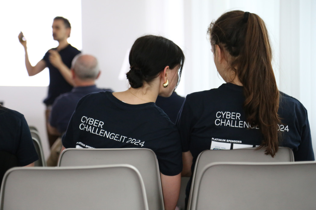 Teilnehmende der Cyber Challenge IT 2024 sitzen im Publikum und hören einer Präsentation zu.