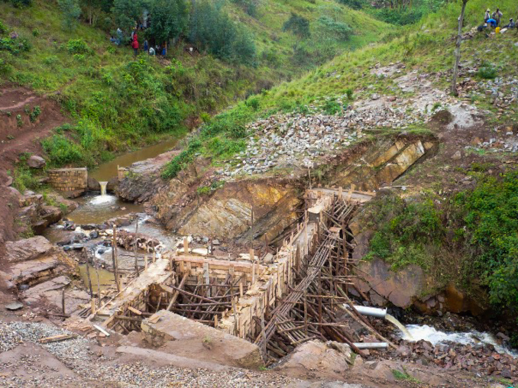 Struttura provvisoria in legno e impalcatura per la costruzione di una diga in un’area collinare verde.