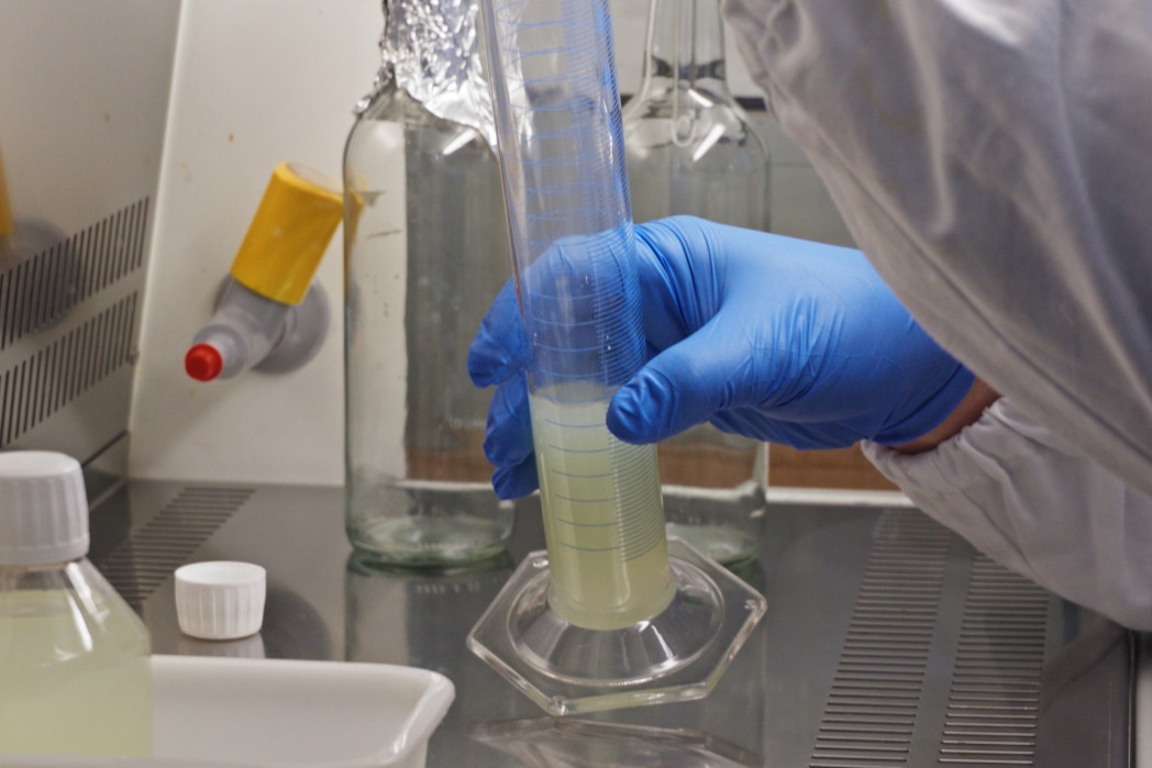 Mano con guanto blu misura un liquido in un cilindro graduato.