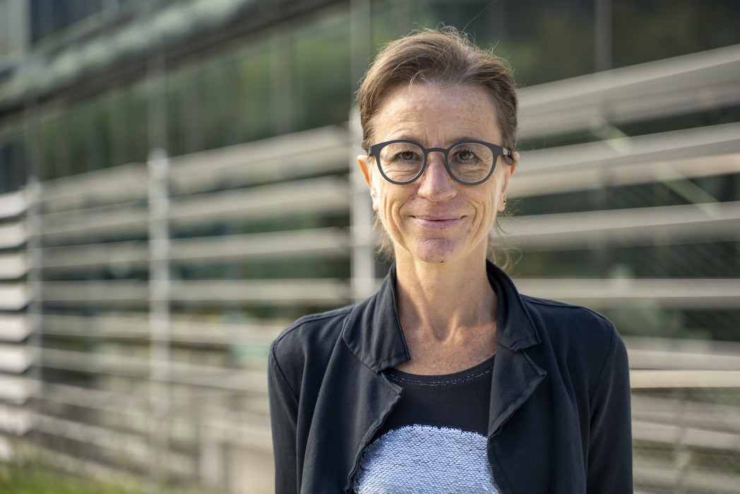 Lächelnde Frau mit Brille vor Fensterfront mit Verkleidungen. 