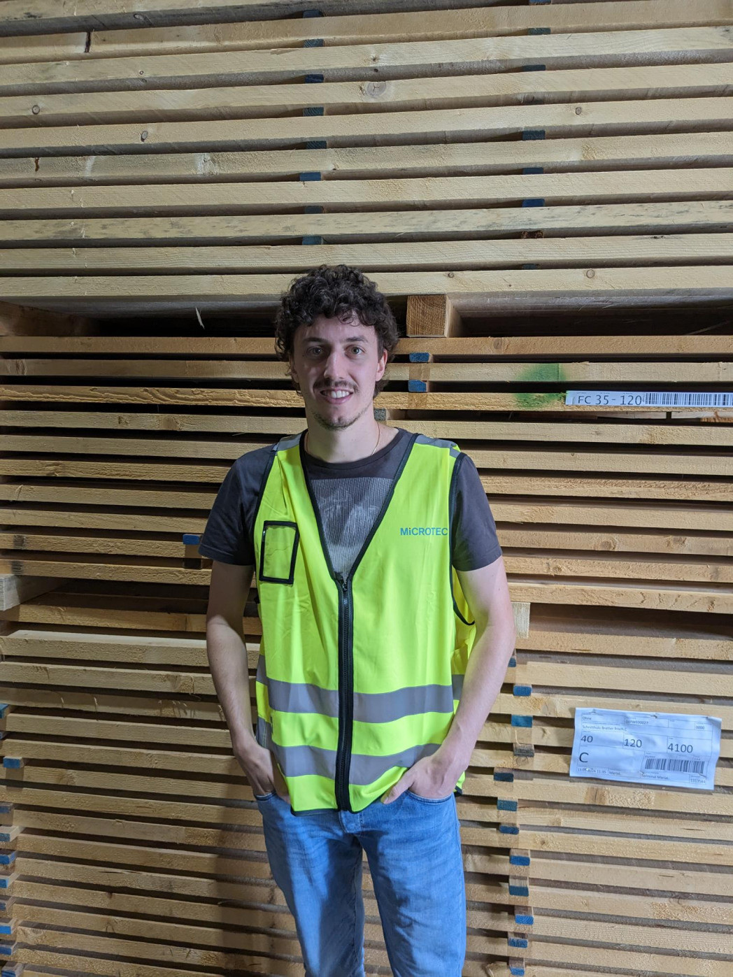 Junger Mann mit Warnweste vor Holzstapel