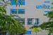 Fassade der Freien Universität Bozen mit Fenstern und Logo sowie einem Baum davor